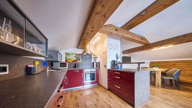A modern kitchen with wooden beams, a central island, and a dining area with a wooden table and chairs. - Apartment Wenger Leogang (Leogang)