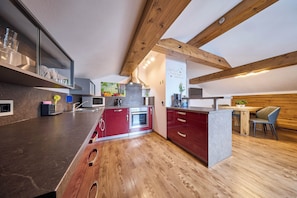 A modern kitchen with wooden beams, a central island, and a dining area with a wooden table and chairs. - Apartment Wenger Leogang (Leogang)