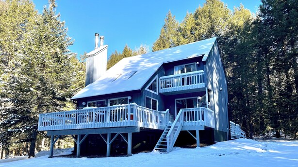 A two-story cabin with a balcony and a chimney, surrounded by a snowy forest.