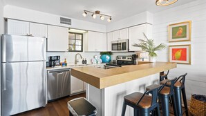 Une cuisine moderne avec des meubles blancs, des appareils en acier inoxydable, un îlot central en bois doté de tabourets et un luminaire suspendu.
