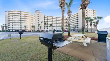 A parking lot with a grill, picnic table, trash bin, and a hotel building in the background.