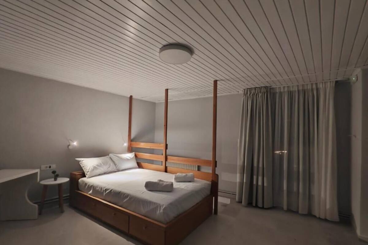 Ein modernes Schlafzimmer mit einem Himmelbett, einem Nachttisch und einem großen Fenster mit Vorhängen.
