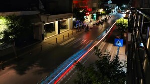 Een verlicht straatbeeld 's nachts, met gebouwen en een zebrapad.