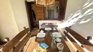 A dining area with a wooden table set for four, including plates, glasses, and cutlery. A wicker lamp hangs above, and a book and a decorative can are on the table. - D1MORA Castello: a PET FRIENDLY corner of peace with shared pool (Gardone Riviera)