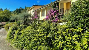 A row of yellow buildings with balconies, surrounded by lush greenery and flowering plants. - D1MORA Castello: a PET FRIENDLY corner of peace with shared pool (Gardone Riviera)