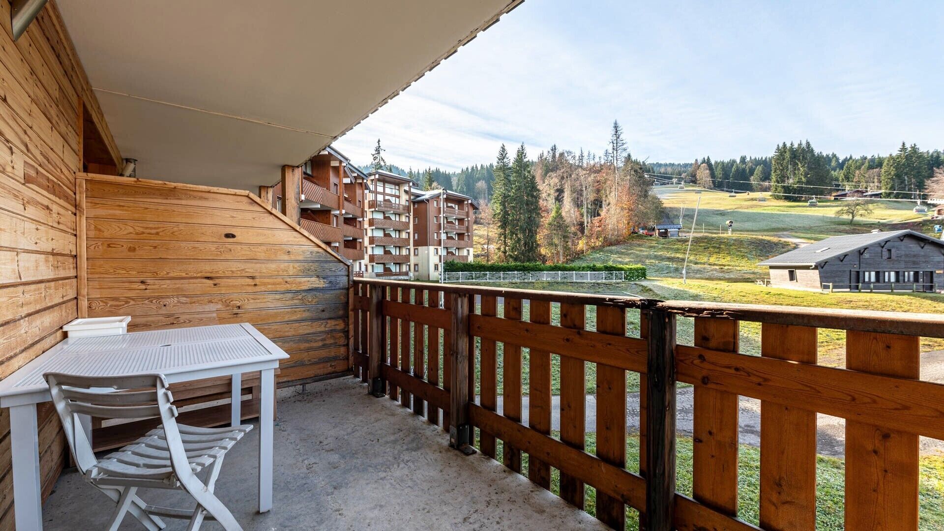 A wooden balcony with a table and chairs, overlooking a residential area with houses and trees.