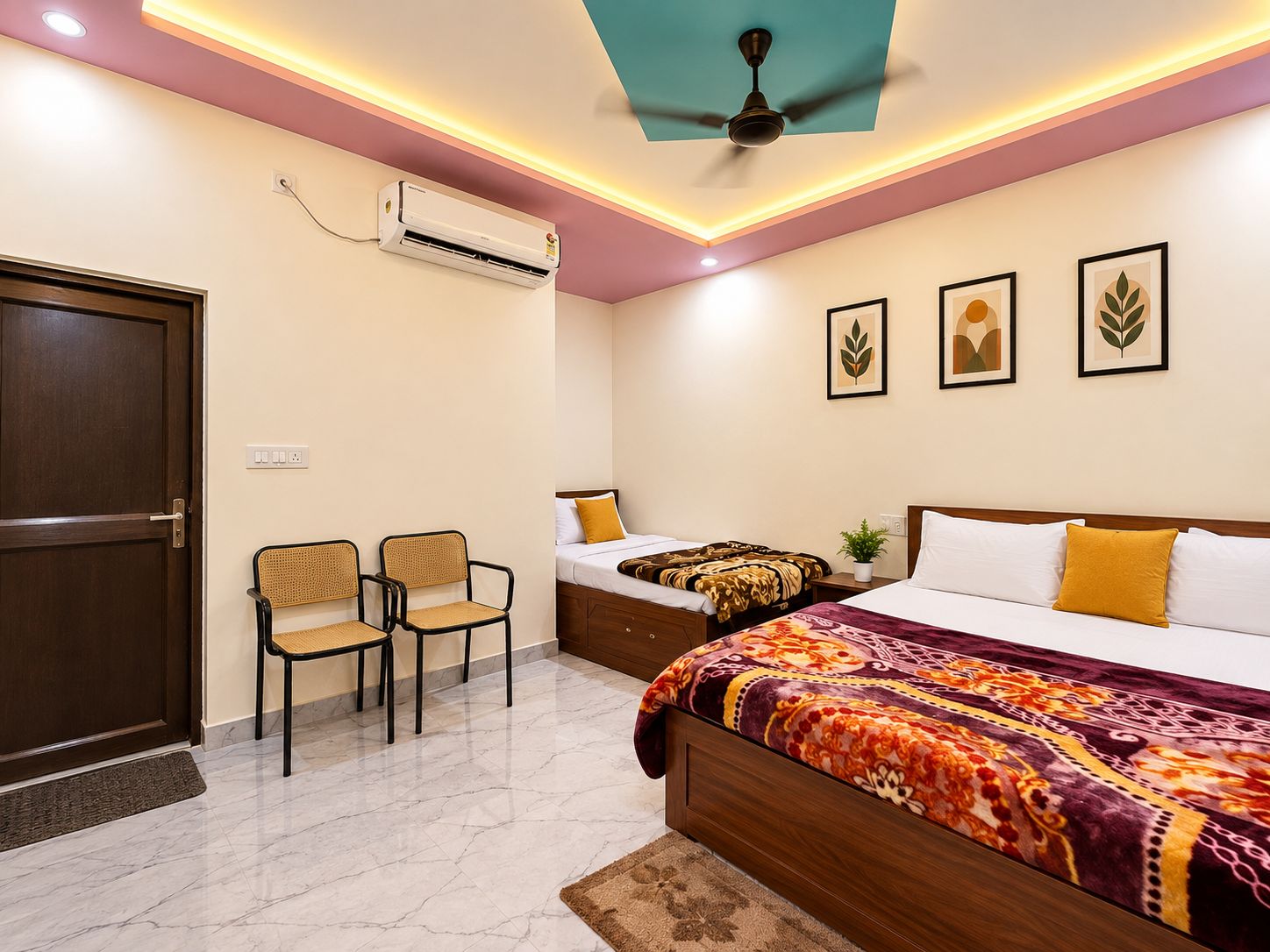 Habitación de hotel con cama, dos sillas, ventilador de techo, aire acondicionado y cuadros en la pared.
