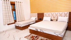 A bedroom with a large bed, a smaller bed, a window with curtains, and a patterned rug.