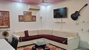 A living room with a white sofa, a glass coffee table, a ceiling fan, a flat-screen TV, and a guitar on the wall.