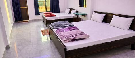 A hotel room with two beds, a small table, a window with curtains, and a door.