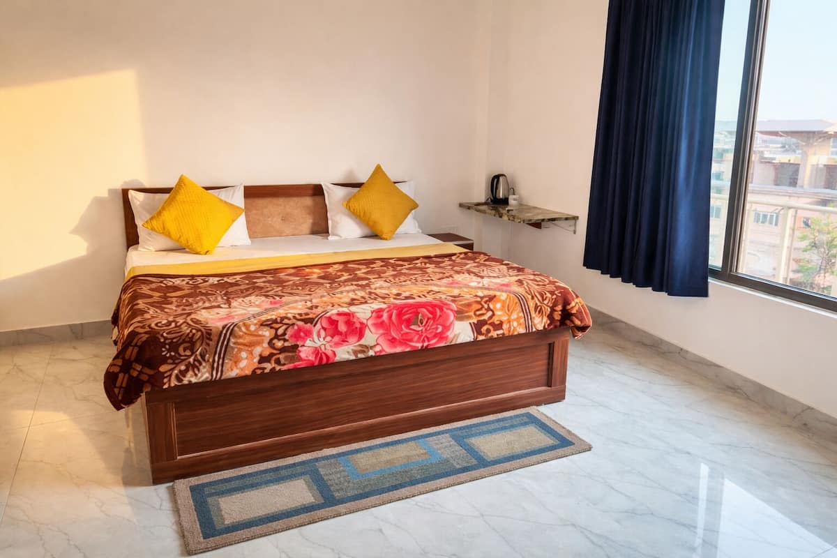 Une chambre à coucher avec un lit, des oreillers, une table de chevet, une fenêtre avec des rideaux et une vue sur les bâtiments à l’extérieur.