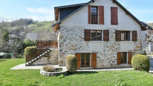 Une maison en pierre avec un escalier, des volets en bois et une pelouse bien entretenue.