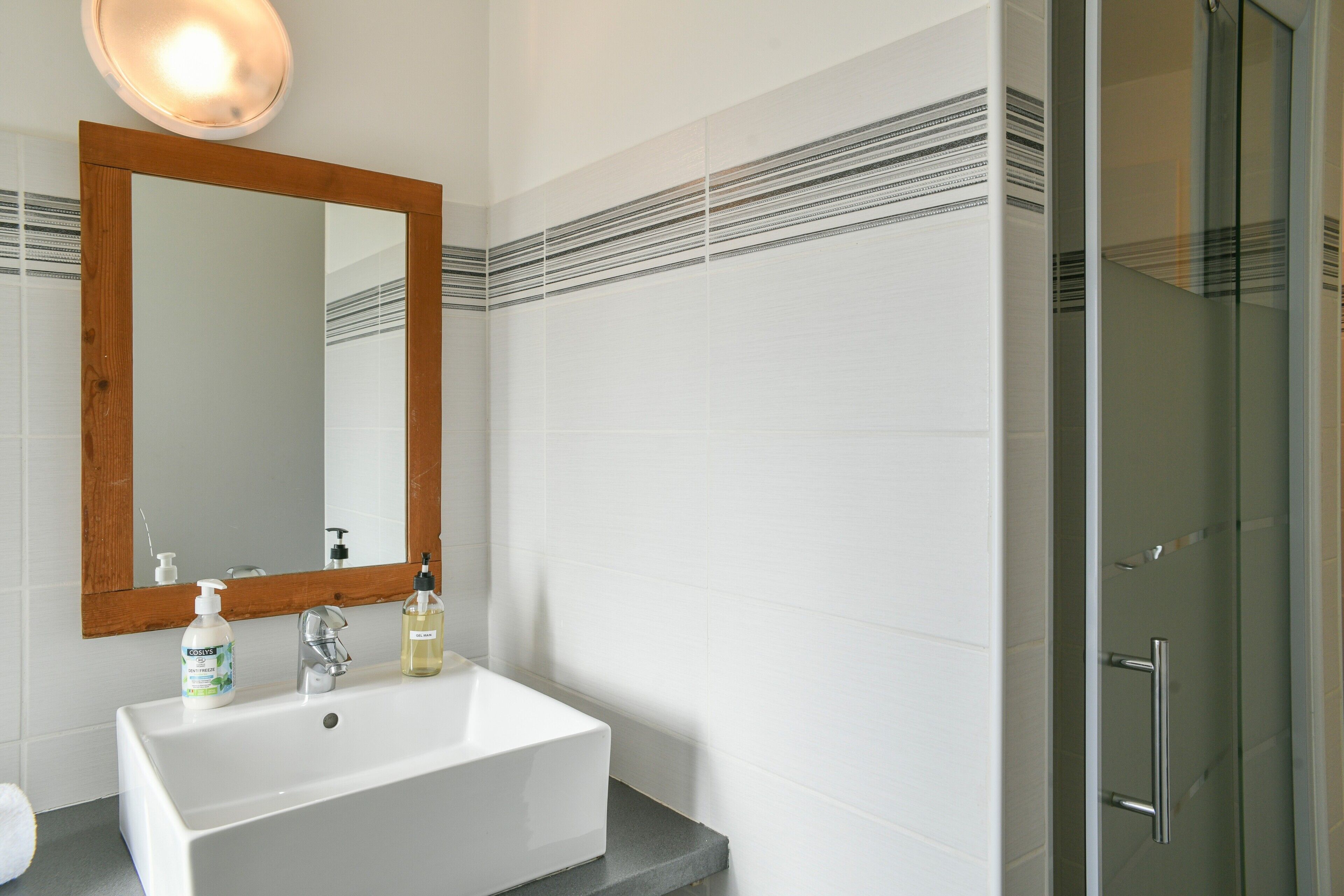 A bathroom with a white sink, a wooden-framed mirror, and a glass shower door.