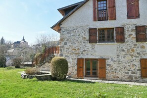 Un bâtiment en pierre avec des volets en bois, un escalier et une pelouse bien entretenue.