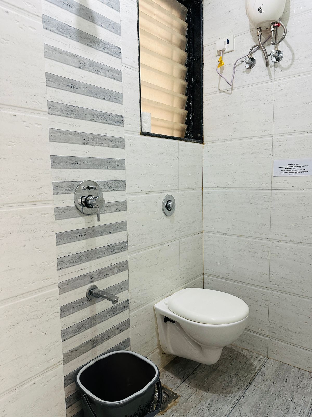 A bathroom with a toilet, a shower, and a bucket.