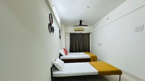 A small, modern room with two single beds, a ceiling fan, and a large window with curtains.
