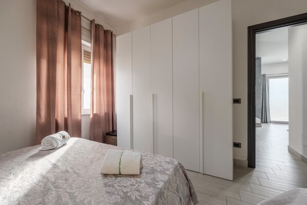 A bedroom with a bed, a wardrobe, and a view of a balcony.