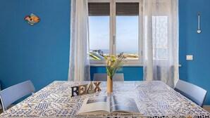 Une pièce avec un mur bleu, une table recouverte d’une nappe à motifs, un livre et un vase rempli de fleurs.