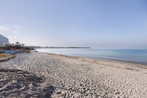 Ein Sandstrand mit blauem Himmel, einer entfernten Küste und Gebäuden links.