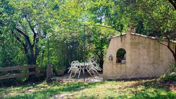 Un espacio de estar al aire libre rústico con una estructura de piedra, rodeado de exuberante vegetación.
