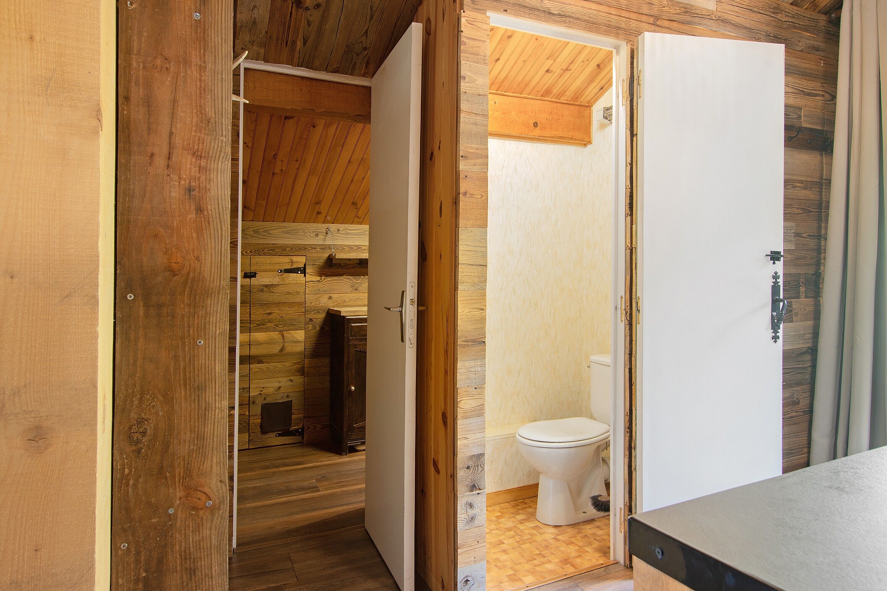 Een houten interieur met een houten deur die leidt naar een badkamer met toilet en douche.