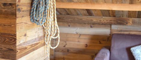 A wooden interior with a rope coiled on a wall, a wooden ceiling, and a couch with a cushion.