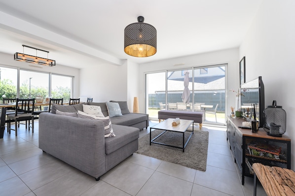 A spacious living area with a grey sofa, a coffee table, and a dining area with chairs and a table.