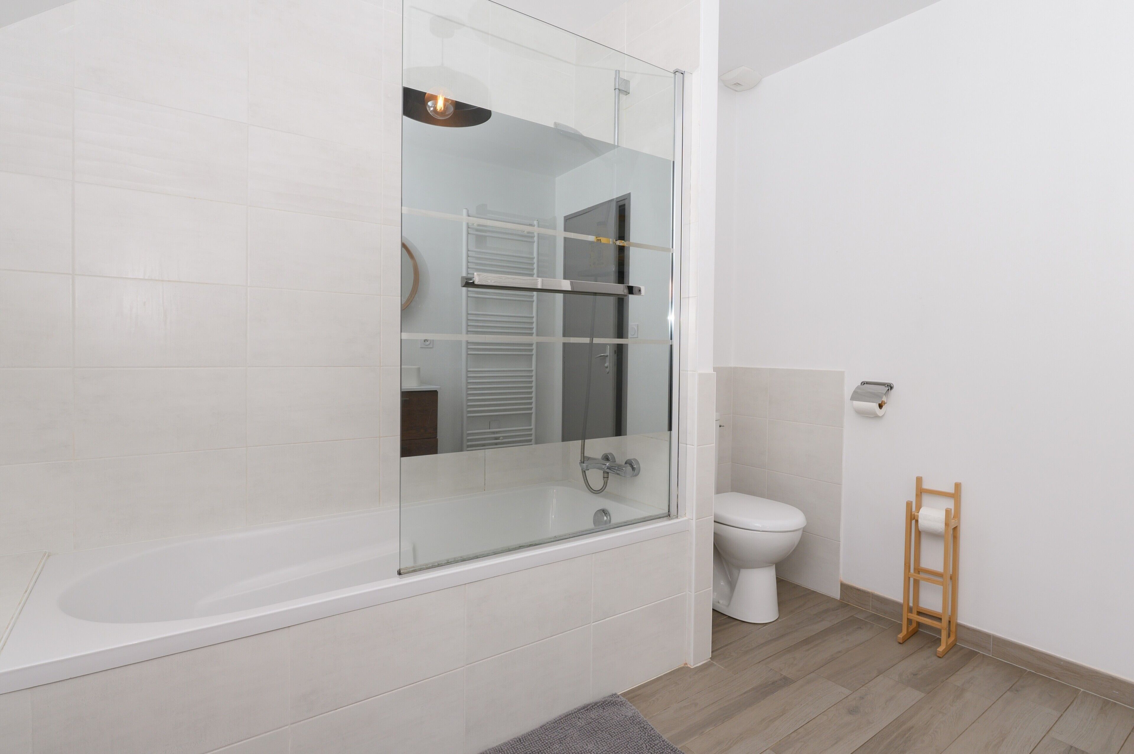 A modern bathroom with a glass-enclosed shower, a toilet, and a wooden ladder for toilet paper.