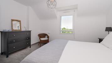 A bedroom with a bed, dresser, chair, window, and geometric pendant light.