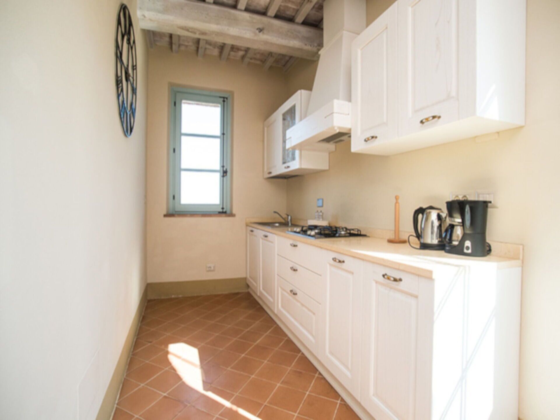 A kitchen with white cabinets, a window, a stove, and a coffee maker.