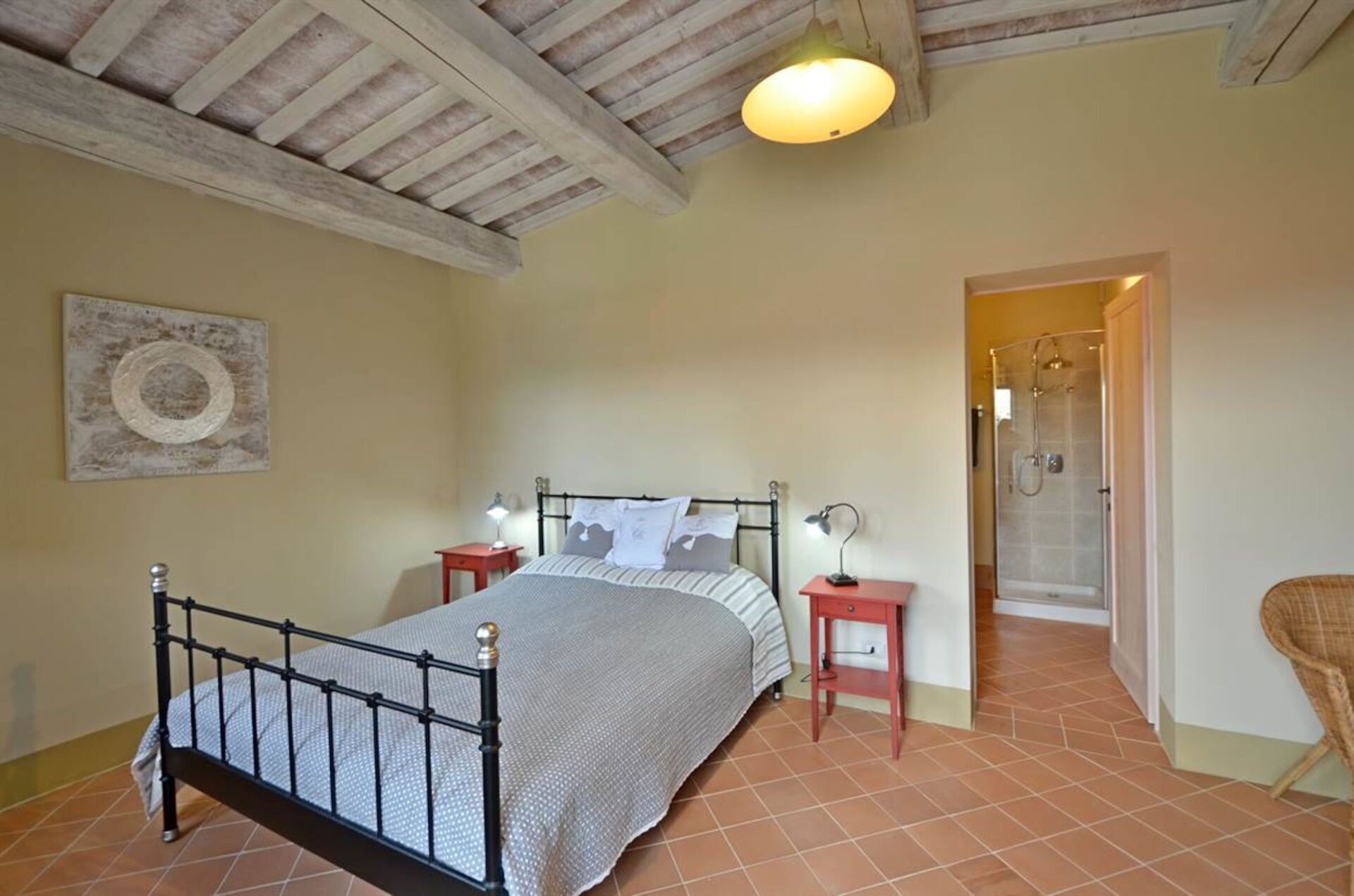 A bedroom with a bed, bedside tables, a lamp, a chair, and a shower area.
