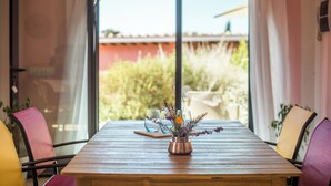 A wooden table with a copper vase of flowers, surrounded by chairs with purple and yellow cushions, in a room with large windows and curtains. - Cosy apartment with A/C, WIFI, pool, TV, terrace and pets allowed, close to Montepulciano (Torrita Di Siena)