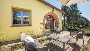 An outdoor patio with wicker furniture, a yellow building, and a brick archway. - Cosy apartment with A/C, WIFI, pool, TV, terrace and pets allowed, close to Montepulciano (Torrita Di Siena)