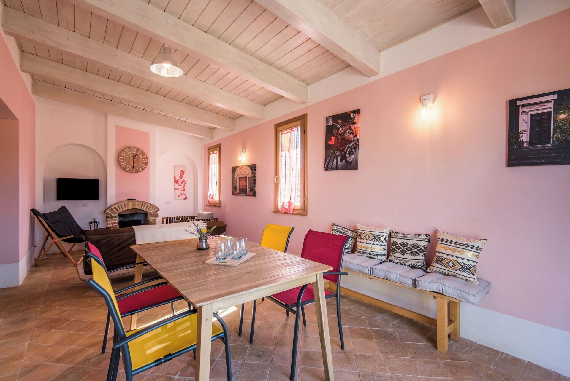 A cozy dining area with a wooden table and colorful chairs, a fireplace, and a seating area with patterned cushions.