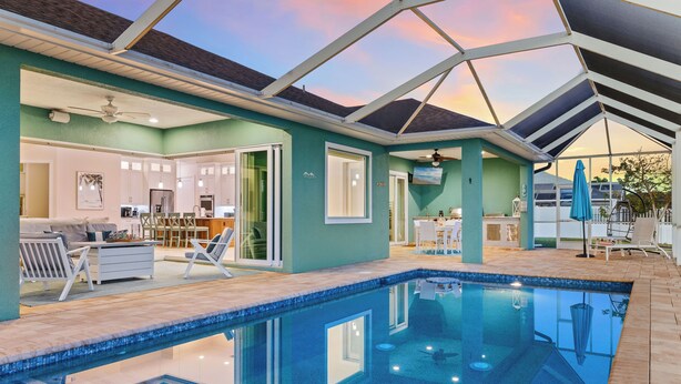 Un área de piscina interior moderna con techo de vidrio, una cocina y un comedor.