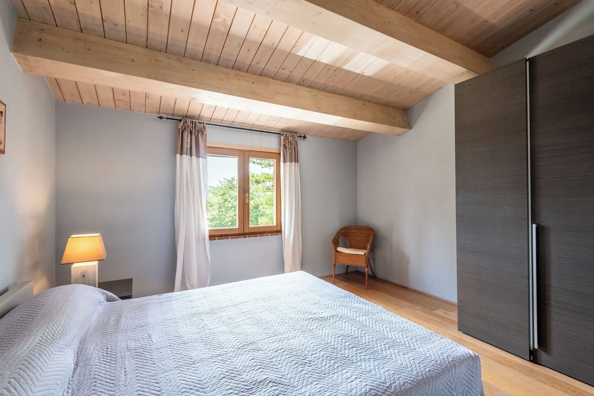 Une chambre à coucher avec un lit, une fenêtre avec des rideaux, une chaise, une lampe et une armoire.