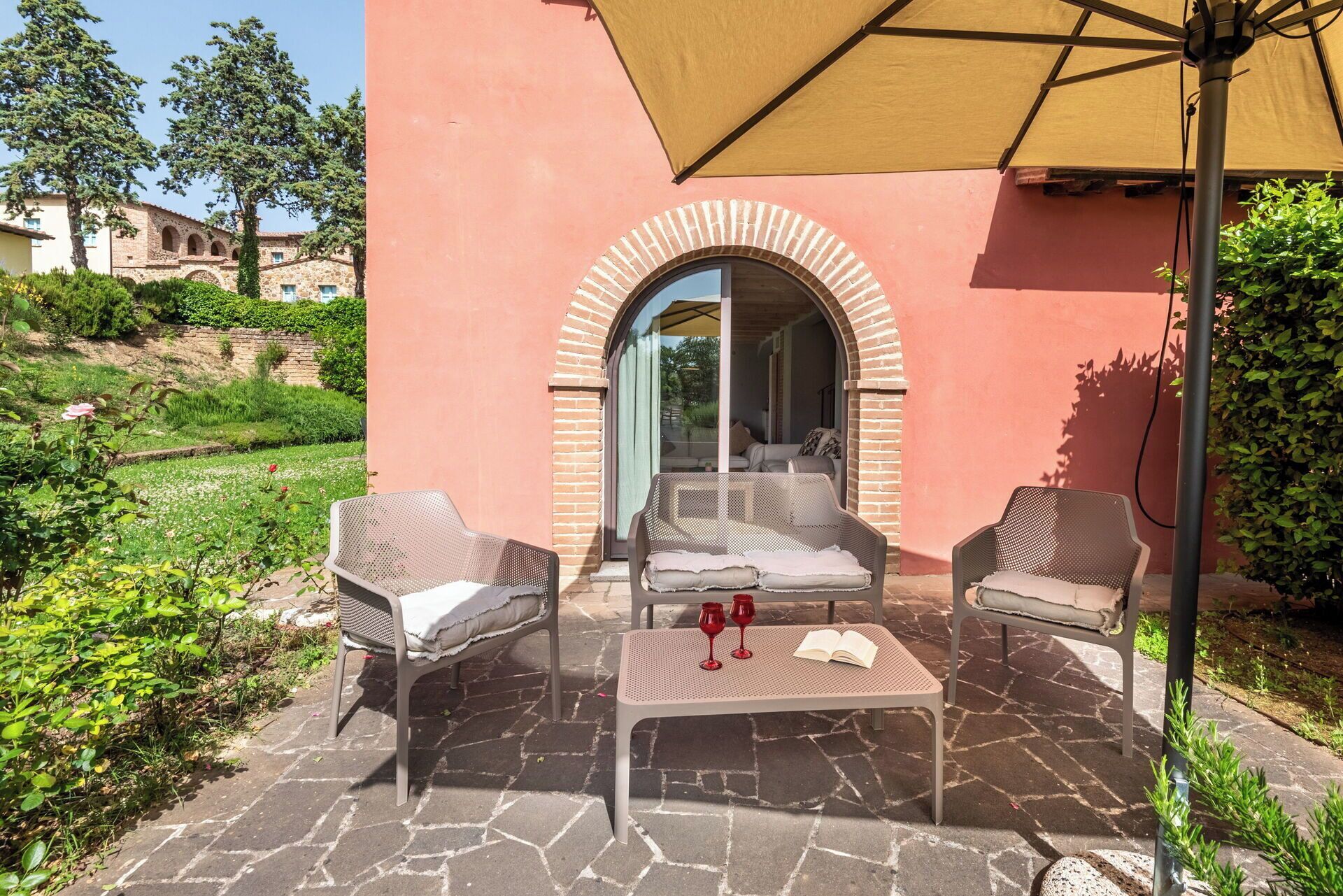 An outdoor seating area with two chairs and a table, a large umbrella, and a view of a building through an arched doorway.