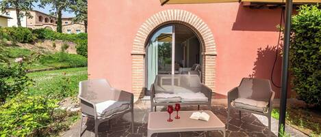 An outdoor seating area with two chairs and a table, a large umbrella, and a view of a building through an arched doorway.