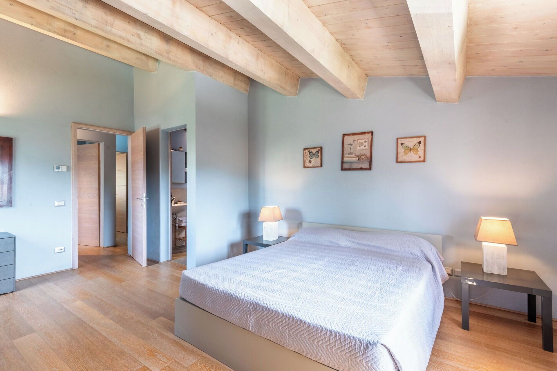 A bedroom with a bed, bedside lamps, a wardrobe, and a door leading to another room.