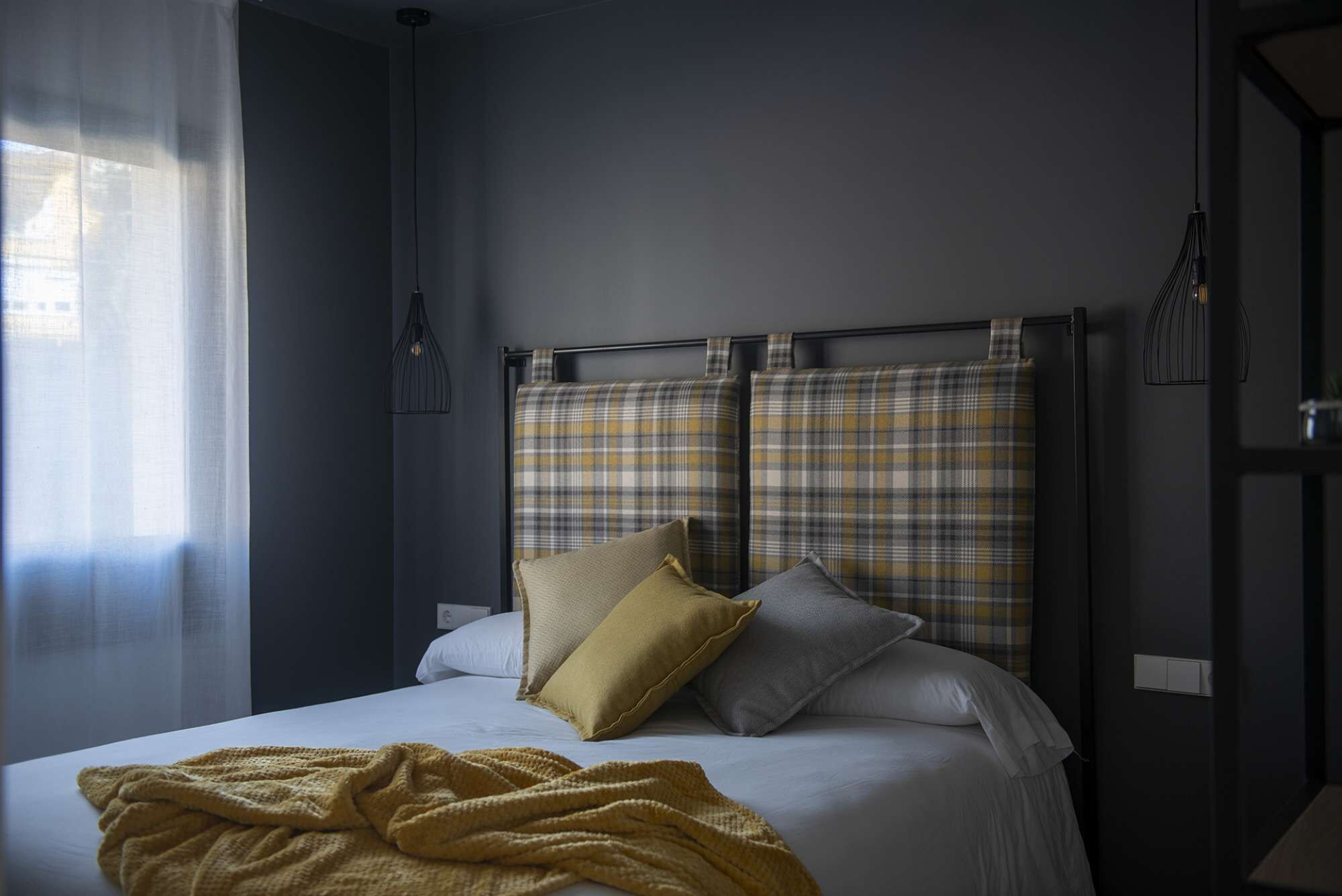 A bedroom with a bed, pillows, a blanket, and a window with curtains.