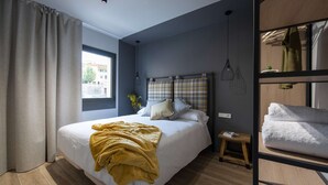 Een moderne slaapkamer met een groot bed, een stapelbed, een raam met gordijnen en een klein nachtkastje.