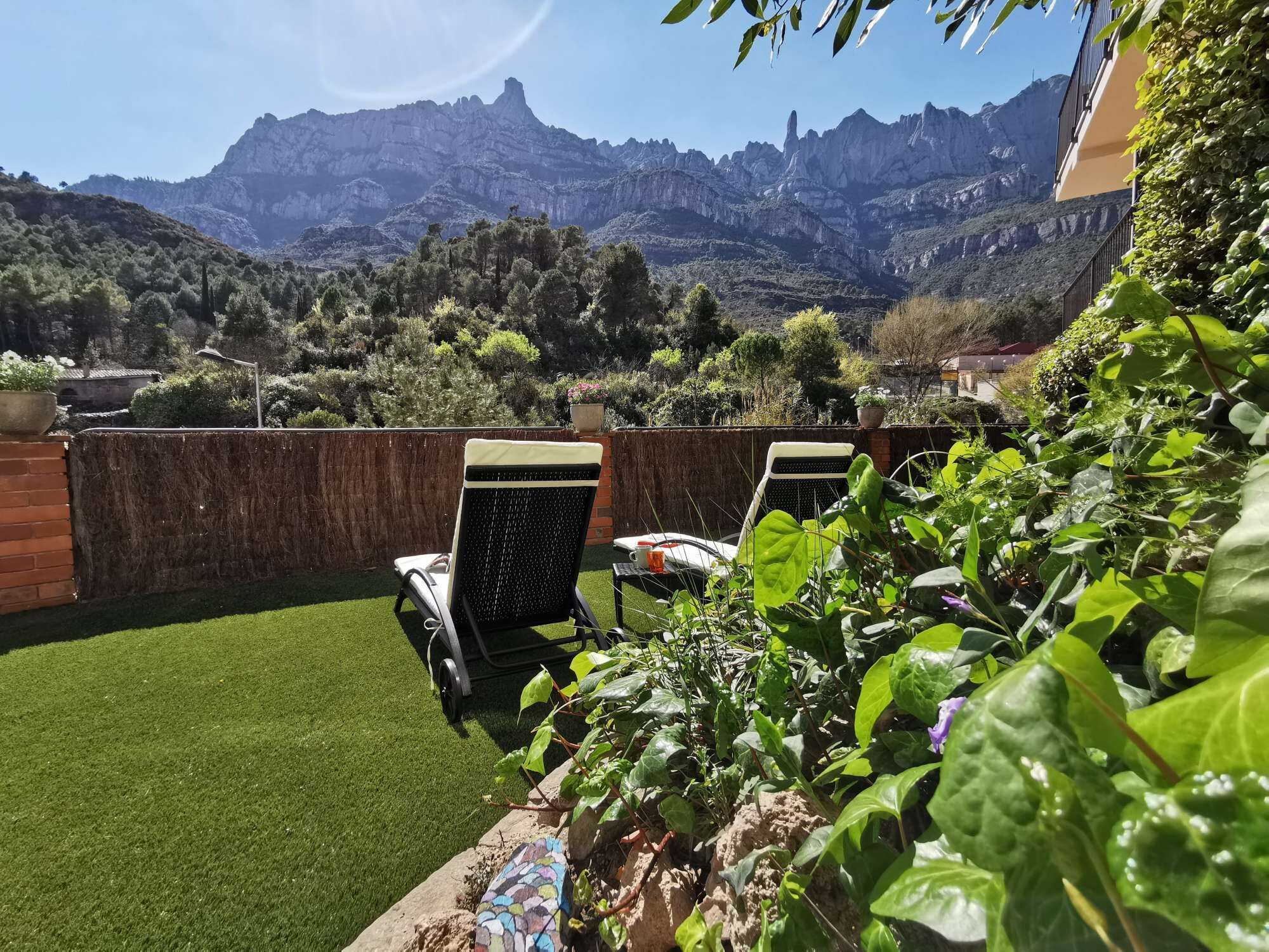 Une terrasse avec un revêtement de gazon synthétique, deux fauteuils en osier et une vue sur les montagnes.