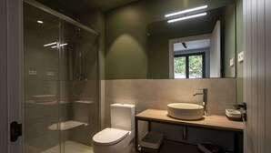 Moderni kylpyhuone, jossa on lasiseinällä varustettu suihku, wc, pesuallas ja peili.