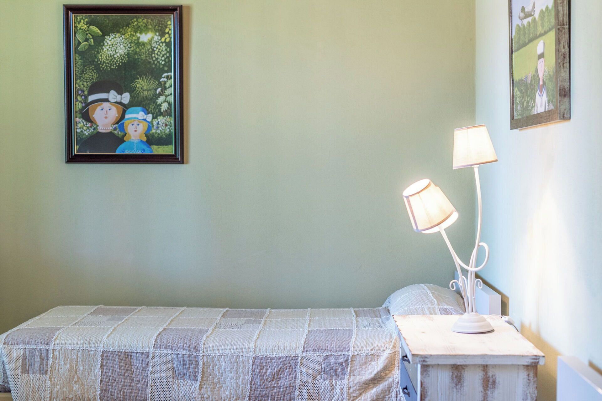 A room with a bed, a nightstand with two lamps, and two framed pictures on the wall.