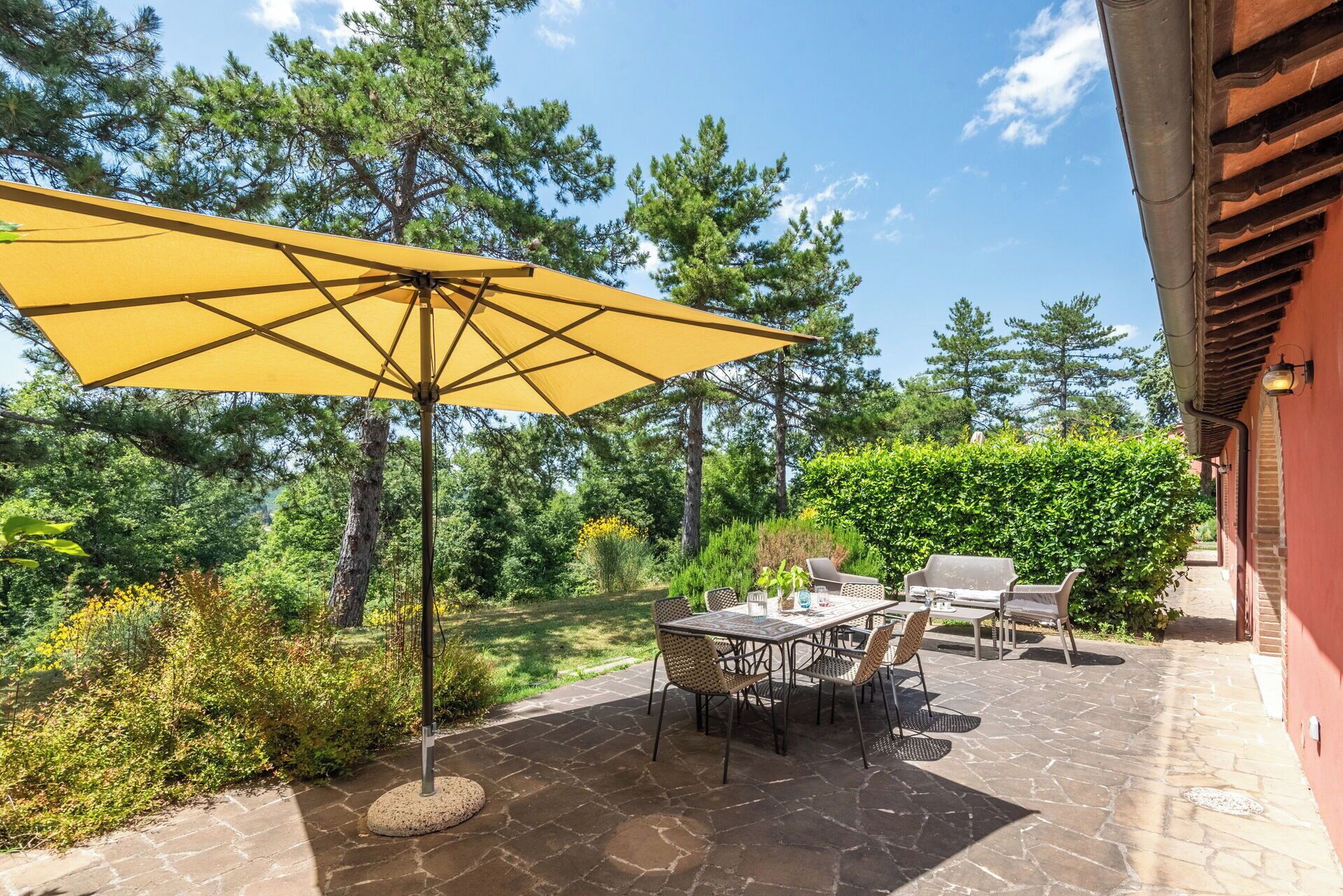 A patio with a yellow umbrella, stone flooring, and outdoor furniture.