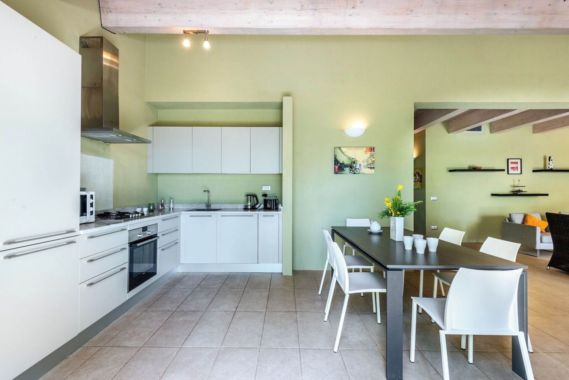 Una cucina moderna con mobili bianchi, un'area pranzo con tavolo e sedie, e un soggiorno con divano e scaffali.