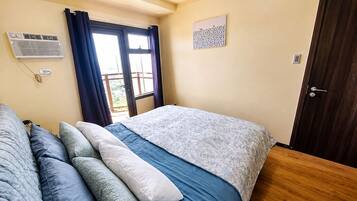 Ein Schlafzimmer mit Bett, einem Fenster mit Vorhängen, einer Tür und einer Wand-Klimaanlage.