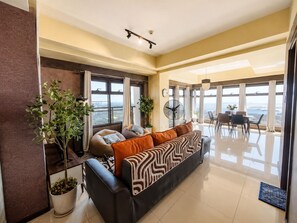 A modern living room with a sofa, a dining area, and a view of the city.