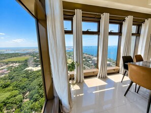 Une chambre située dans un immeuble de grande hauteur, dotée d’une grande fenêtre donnant sur un paysage côtier.