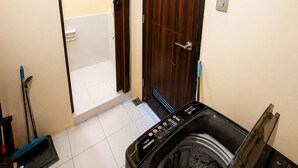 A laundry room with a washing machine, a mop, and a broom.
